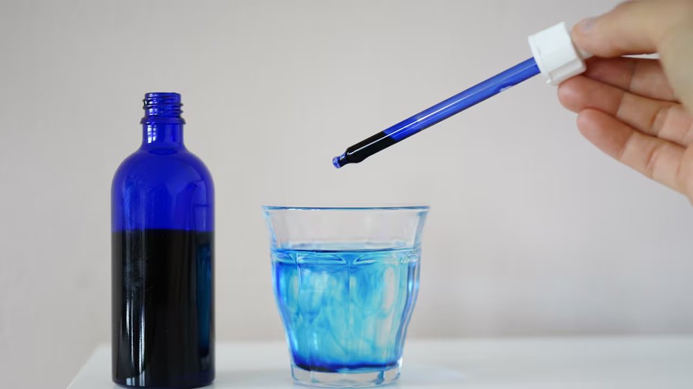 Synthetic blue dye being dropped into a glass of water